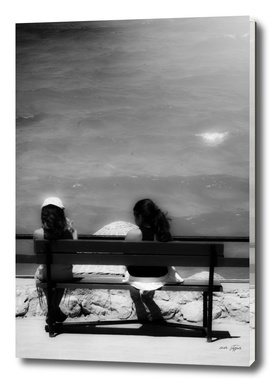 Two girls sitting on a bench at sea side