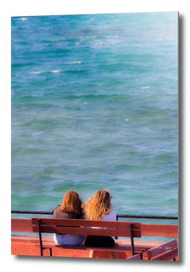 Two girls sitting on a bench at seaside