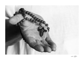 Hand of an old woman holds rosary while praying