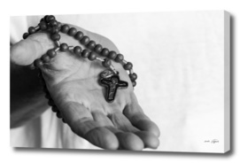 Hand of an old woman holds rosary while praying
