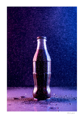 Glass bottle with carbonated drink under the drops of water
