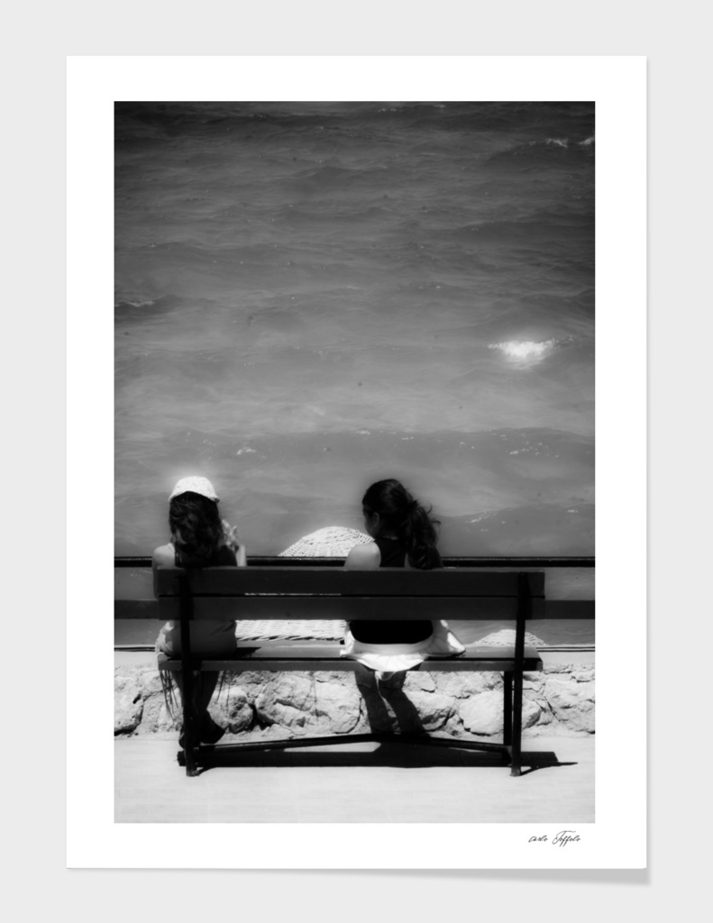 Two girls sitting on a bench at sea side